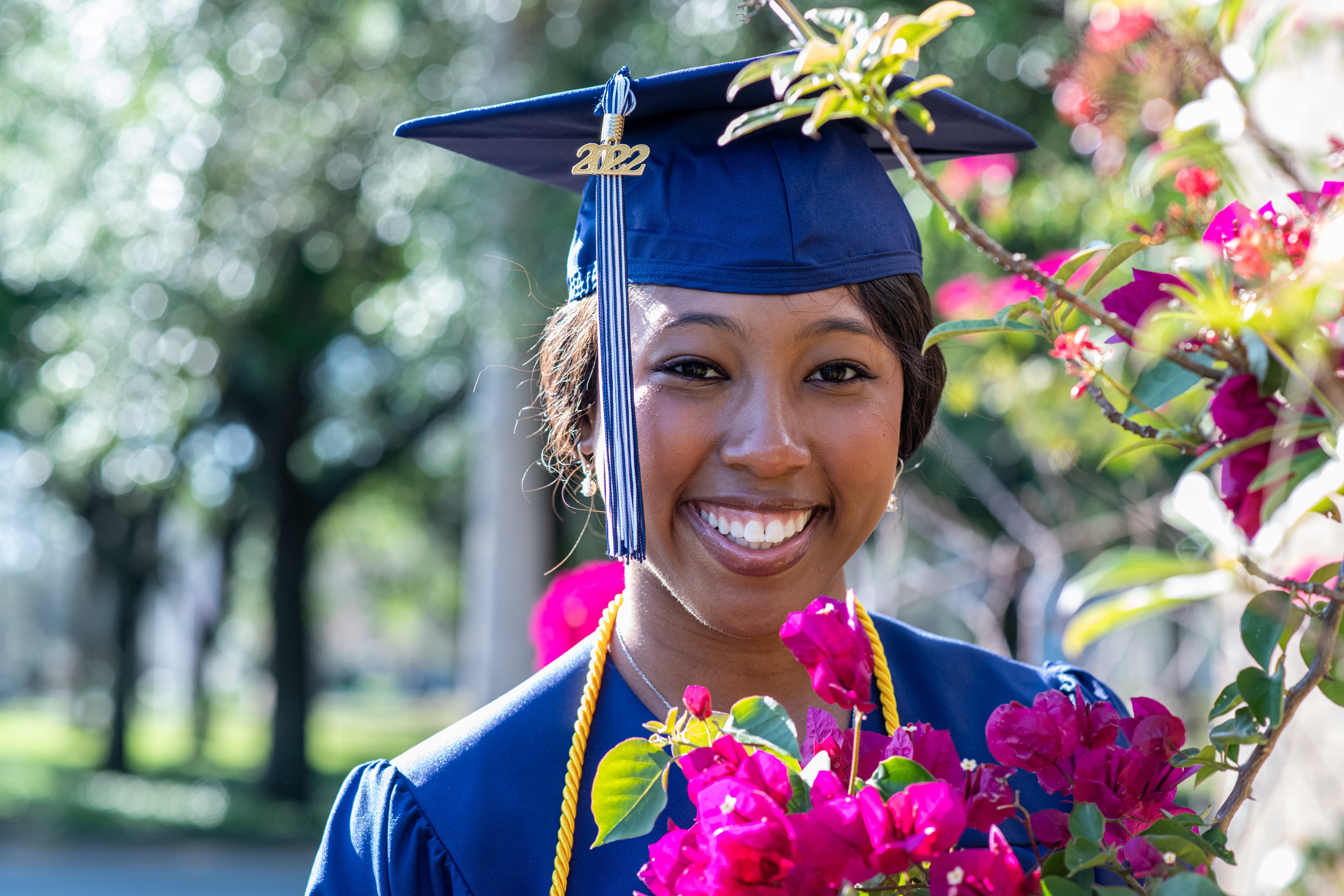 Graduate in cap and gown smiling among flowers