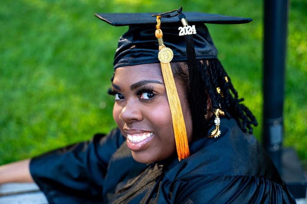 Graduate in cap and gown smiling outdoors with gold tassel